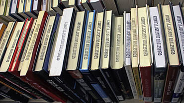 A row of books on a book cart, showing the Georgetown University Library stamped on the top of the pages