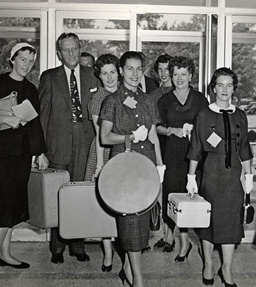 Black and white photograph of nursing students carrying suitcases and hatboxes.