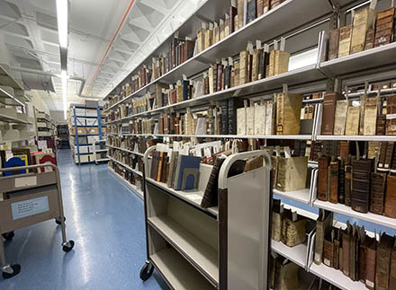 A book cart with a shelf full of rare books in an aisle of the Special Collections vault