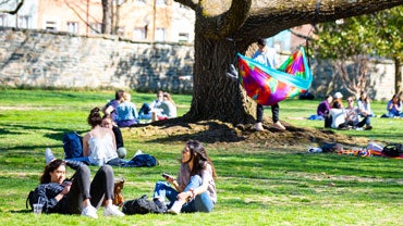 Students relaxing on Healy Lawn, including one in a colorful hammock hanging from a tree.