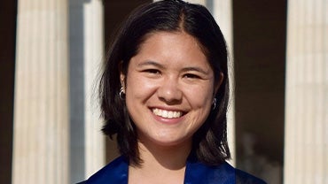 A young woman smiling wearing a blue suit in front of white columns.