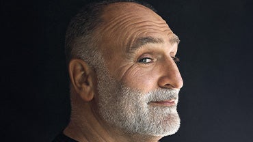 Jose Andres, a bald bearded man, looks to the right on a gray backdrop, his gaze toward the lens.