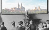 A professor lectures in a classroom with an image of the Georgetown skyline behind him showing Healy Hall and Lauinger Library