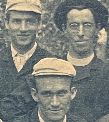 Three men in 1890s period clothing, all three with hats, one with spectacles