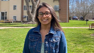 Prachi Shah, a young Indian woman wearing glasses, smiles on a grassy yard.