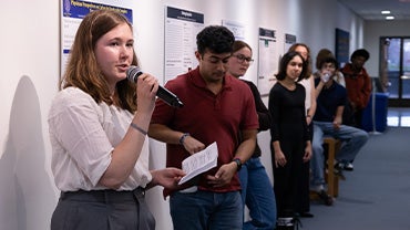 A female student presents her work alongside others standing beside their research posters.