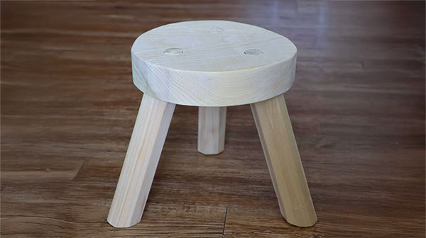 a three legged stool made out of a light colored wood