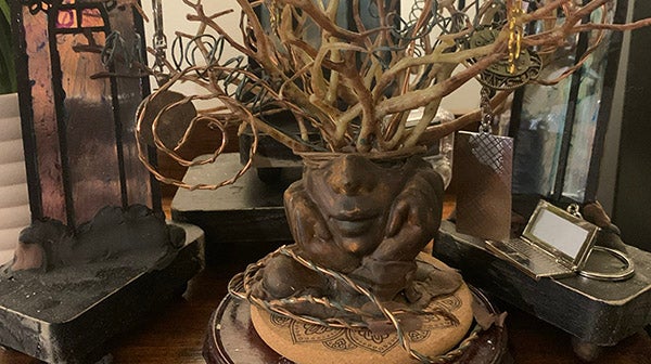 Small branxches grow out of a sculpture of a person's head, decorated by pieces of copper wire
