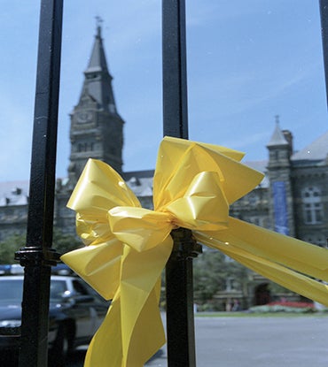 Color photo of yellow ribbon on the main gates with Healy Hall and a blue sky seen in the backgound