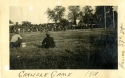 a black and white potograph of two men sitting on a football field opposite a large group of spectators in the stands. a caption written in ink below the photograph reads "Carlisle Game, 1911"