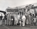 a black and white photograph of Members of the 1949 Georgetown Football Team standing with mascot Butch (a dog) in front of an airplane and below a banner that reads, "georgetown", 1949