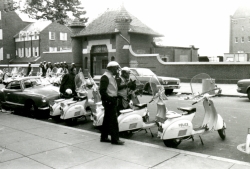 Black and white photograph of policemen wearing gas masks with their scooters across the street from the Prospect Street entrance to the Car Barn