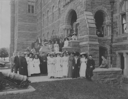 Black and white photograph showing young women from the Visitation Academy posed in front of Healy hall with GU students and faculty. Most of the women are wearing elaborate hats