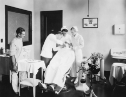 Black and white photograph of dental student treating a patient watched by a faculty member