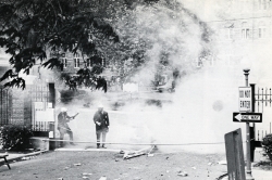 Black and white photograph showing tear gas and police in gas masks at the main gates