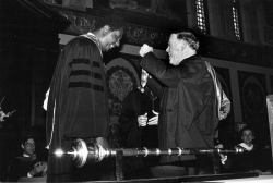Black and white photograph showing GU President Tim Healy about to place the President's Medal around the neck of Coach Thompson