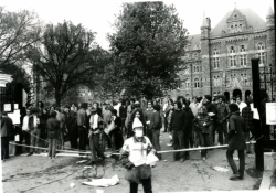 Black and white photograph student medic standing in front of a crowd at the main gates