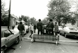 Black and white photograph of protesters on 37th Street just south of the main gates, with a blockade fashioned from a park bench