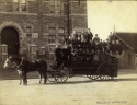 A black and white photograph of Fans heading to the Thanksgiving game. A horse drawn carriage filled with young men stands in front of Healy Hall.