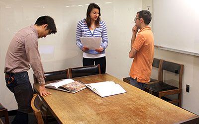 Three students stand around a table in a group study room