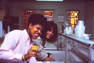 Image of two women, one white and one black, smiling as they scoop ice cream from a freezer while working at the Cone Zone.