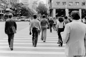 Black and white photo of a group of people crossing the street in downtown Rio during the day. Their backs are to the camera.