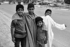 Black and white photograph of 4 young Iraqi boys by the side of the road.  In Mr. Salih's interview he says that the boys,  "sold chewing gum to the few drivers on the street during a coronavirus curfew. They were happy, and laughed all the time."