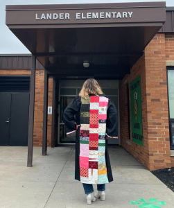 Photo of the artist, Lauren Jacobson, walking into her elementary school wearing the quilted graduation robe.