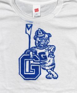 A white t-shirt with a print of a dark blue English bulldog standing and leaning against a large letter "G". He is wearing a sweater and hat with the Georgetown G on it and holding an oar.  