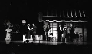 Black and white photograph of select cast members of the 1957 Senior Show "The Most Happy Jet." The cast are assembled in several small groups outside the setting of a cafe.