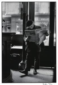 Man standing reading newspaper wearing beret.