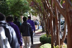 Group of students walk on sidewalk lined with trees, going from Freedom House to waterfront