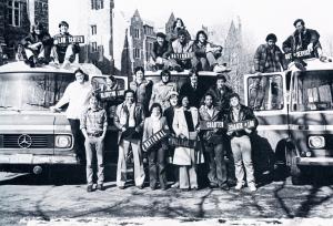 Members of GUTS posed in front of and on three GUTS buses