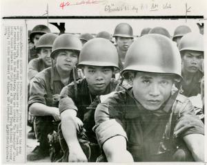 Black and white photo of several Vietnamese soldiers seated in a linear formation wearing helmets. The one in front looks upward.