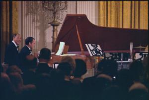 Color photo of President Richard Nixon with Duke Ellington at a grand piano; audience at foreground and candelabra in background