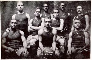 B X W old photo of 9-member basketball team with all members wearing sleeveless tanks and shorts; man at center holding basketball identifying them as members of 1909-10 YMCA team