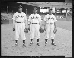 B X W photo of 3 Black baseball players, all wearing uniform identifying them as member of the Grays, on baseball field