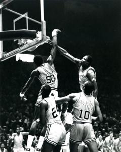 B X W photo of Georgetown basketball center Patrick Ewing dunking basketball over defending center University of Virginia Ralph Sampson whose hand is stretched out; two players in foreground; crowd in background