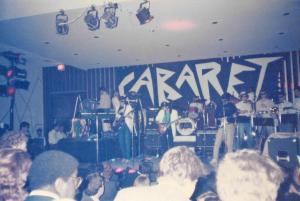 Color snapshot of band playing on a stage with the word Cabaret in white letters behind them