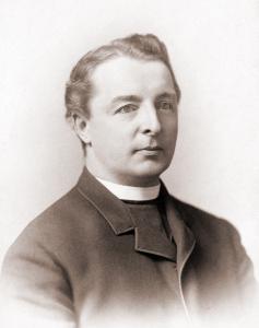 Alphonse Coppens, a young priest with dark wavy hair, wearing a dark coat and a white collar