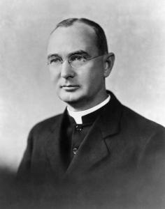 Arthur O'Leary, a middle aged priest with a receding hair line and glasses wearing a dark coat and white collar