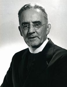 Francis Byrnes, an older priest with thinning hair and rimless glasses, wearing a dark coat and tall white collar