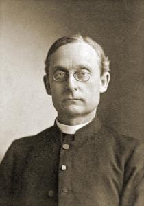 Joseph Havens Richards, a middle aged priest with neatly parted hair wears a dark jacket, white collar, and pince-nez style glasses
