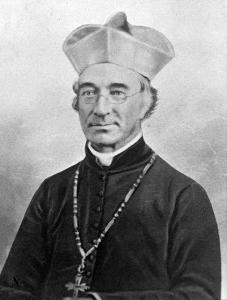 James Van de Velde, an older man with glasses wearing a Jesuit biretta, dark robes, white colar, and large necklace with a cross