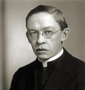 Wilfrid Parsons, a middle aged priest with short carefully parted hair and rimless glasses, wearing a dark coat and white collar