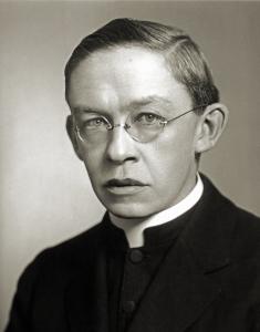 Wilfrid Parsons, a middle aged priest with short carefully parted hair and rimless glasses, wearing a dark coat and white collar
