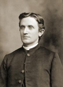 William Clark, a young priest with dark wavy hair, wearing a dark coat and white collar.