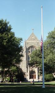 Color photograph showing Copley lawn with White-Gravenor Hall in the background and the flag pole and the flag at half-staff in the foreground.