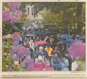 Color newspaper photograph showing people gathering on campus wearing raincoats and carrying umbrellas.