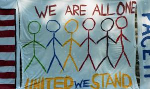 Color photograph showing a decorated bedsheet with the words "We are all one - United we stand."